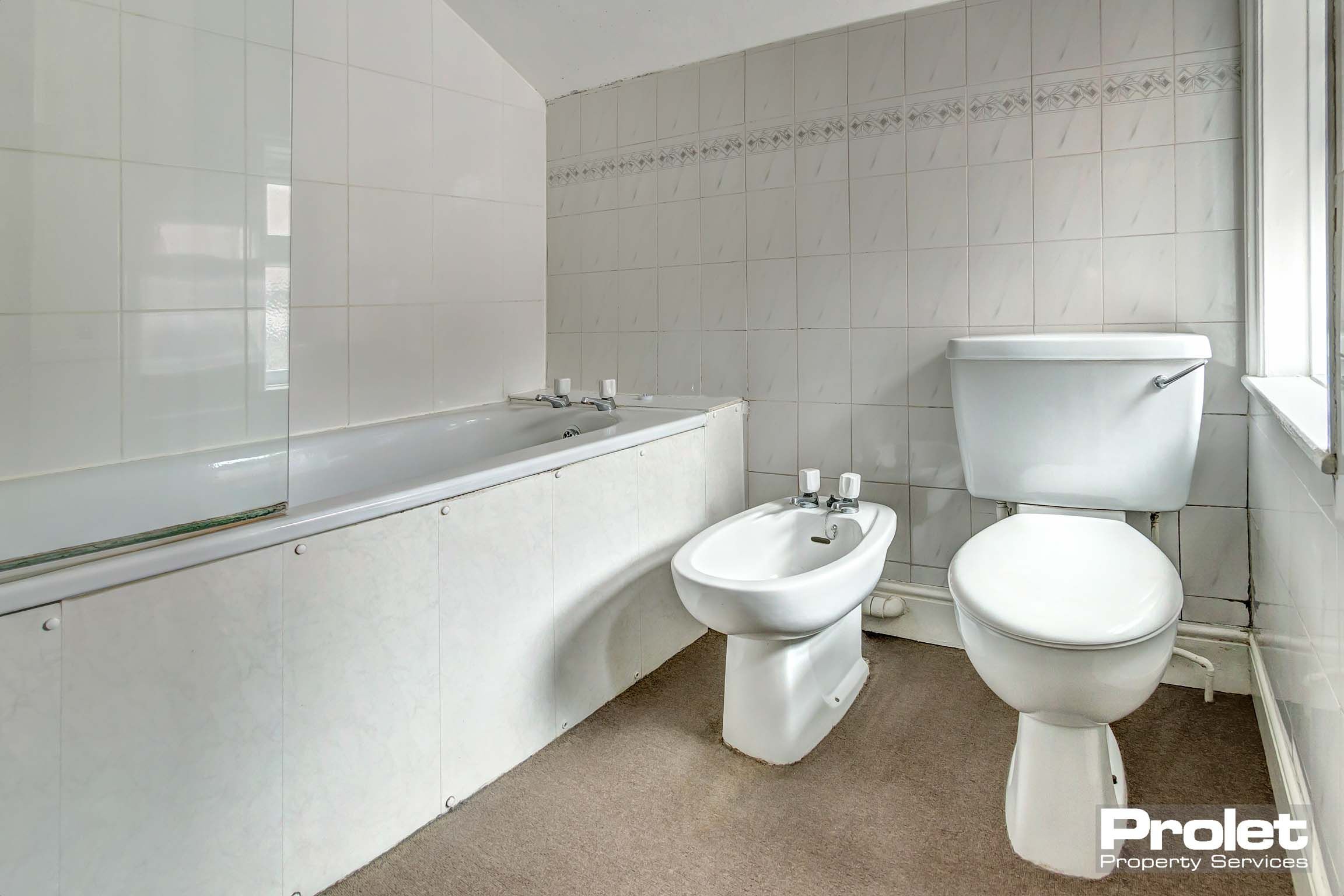 Tiled bathroom with white toilet, sink and bathroom with glass splashguard for shower above.
