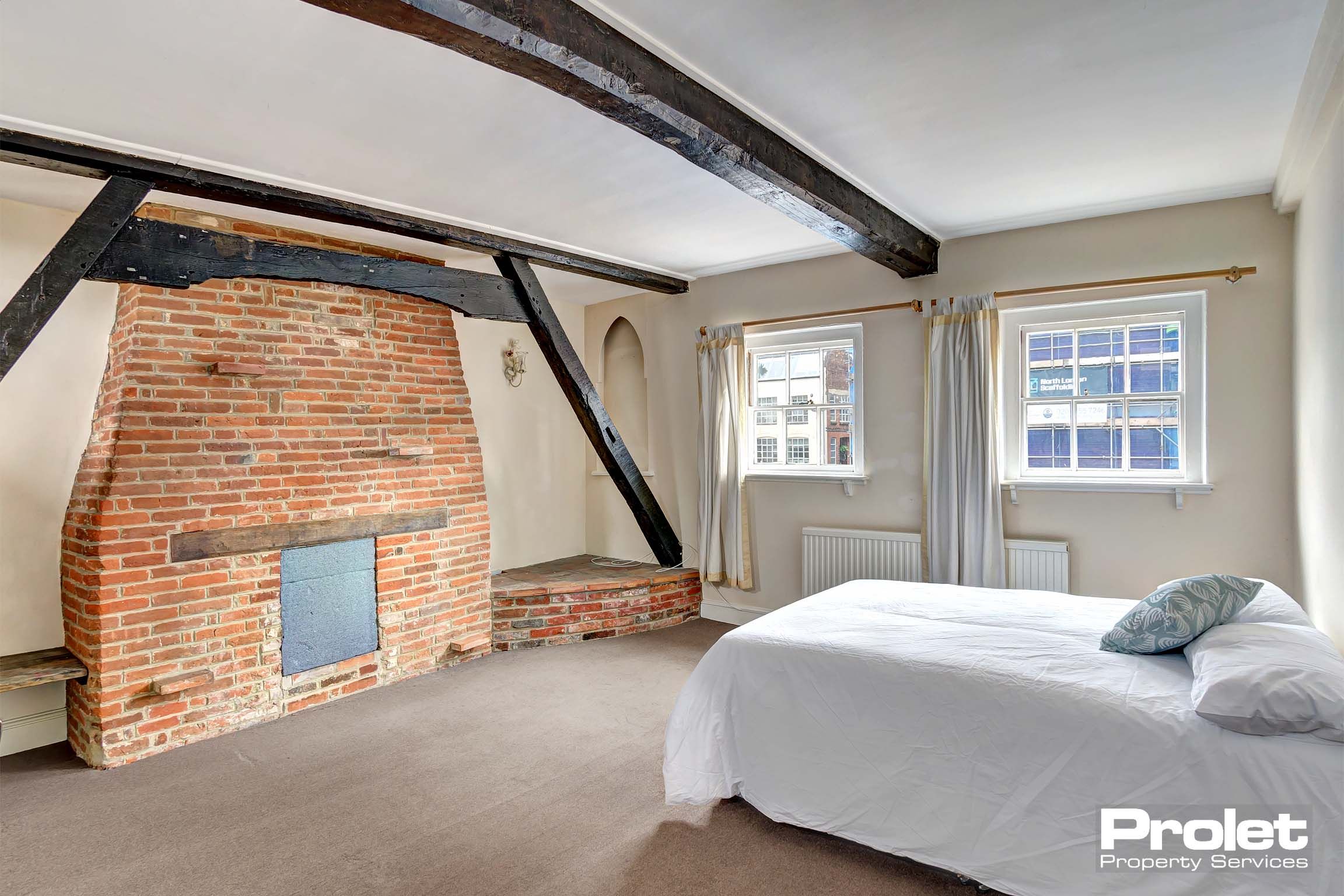 Large double bedroom with black painted beams and a brick chimney stack.
