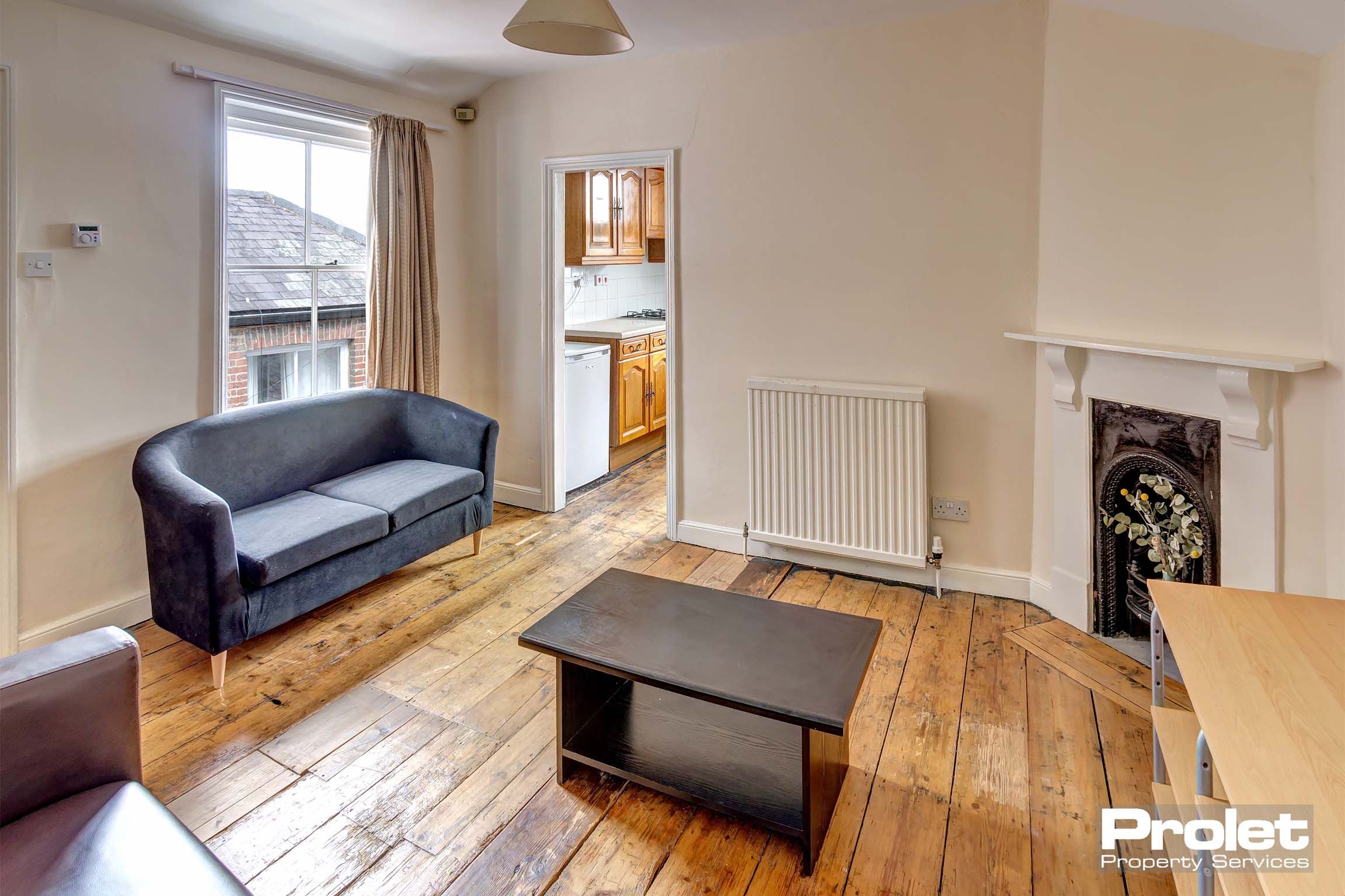 Lounge area with magnolia walls, wooden flooring and a decorative fireplace. One black leather sofa and one brown leather sofa and a black coffee table.