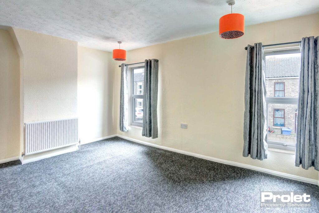 Large front double bedroom, with two windows, grey carpets, and cream walls.