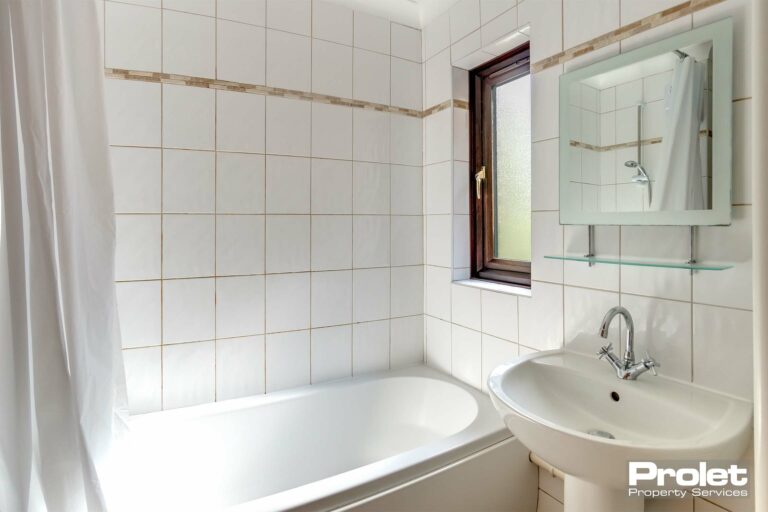 Bathroom with shower over white bath with white suite and tiles