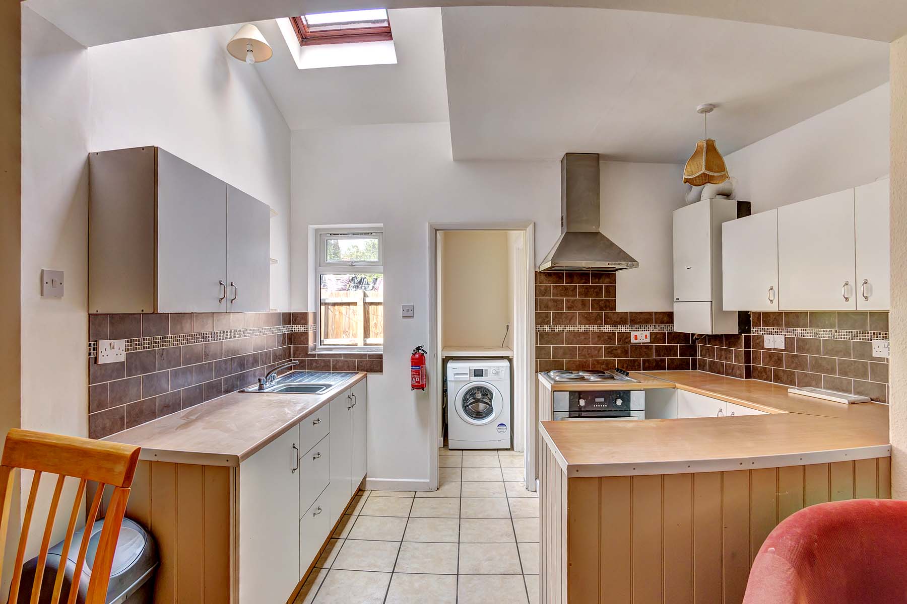 Kitchen with wooden worktops, white cabinets, white goods, tiled floor, and skylight