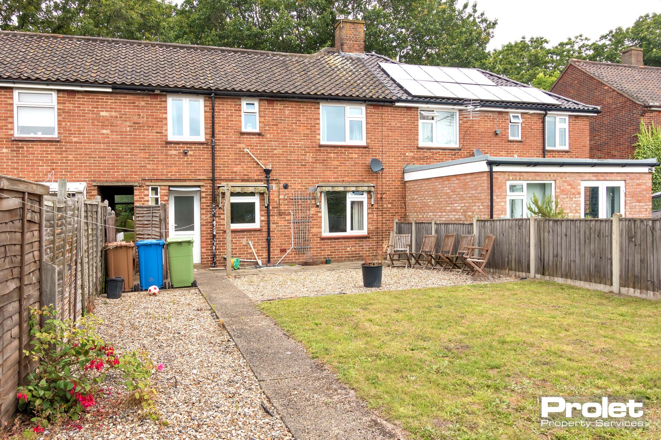 Rear view of the house, garden space with grass area and a concrete pathway.