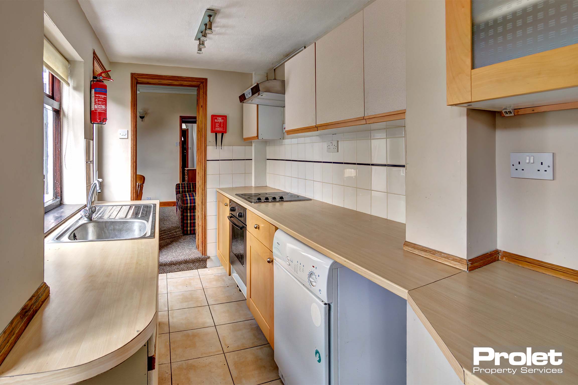 Long galley kitchen with white cabinets, wood effect worktops, and white goods.