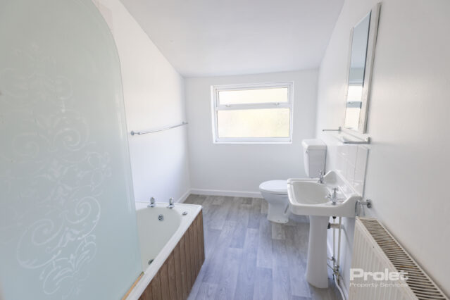Bathroom with shower over bath, sink, toilet, and lino flooring
