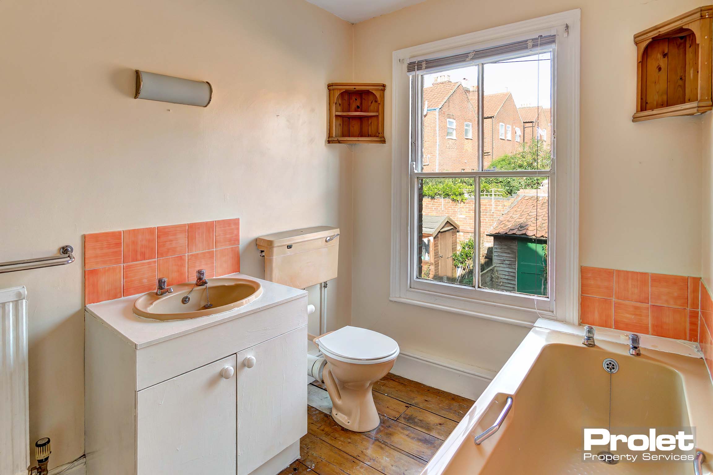 Bathroom with peach suite, pink tiled splashback, and wooden floor