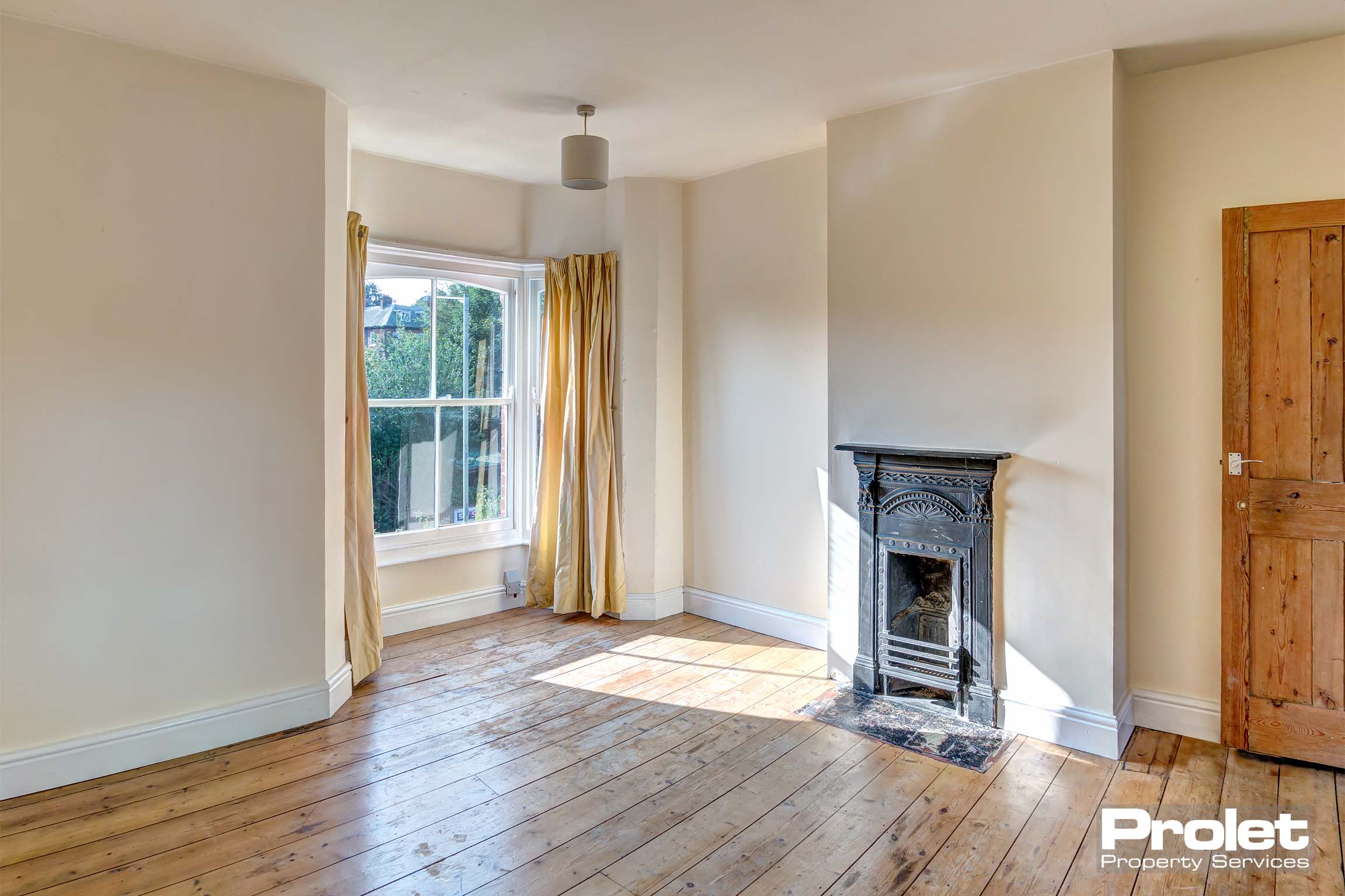 Bright bedtoom with bay window, hardwood floor, and period fireplace