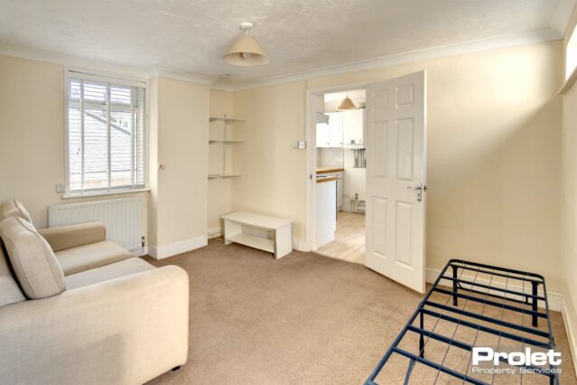 Brown carpet, magnolia walls, beige sofa, single metal bedframe and TV unit