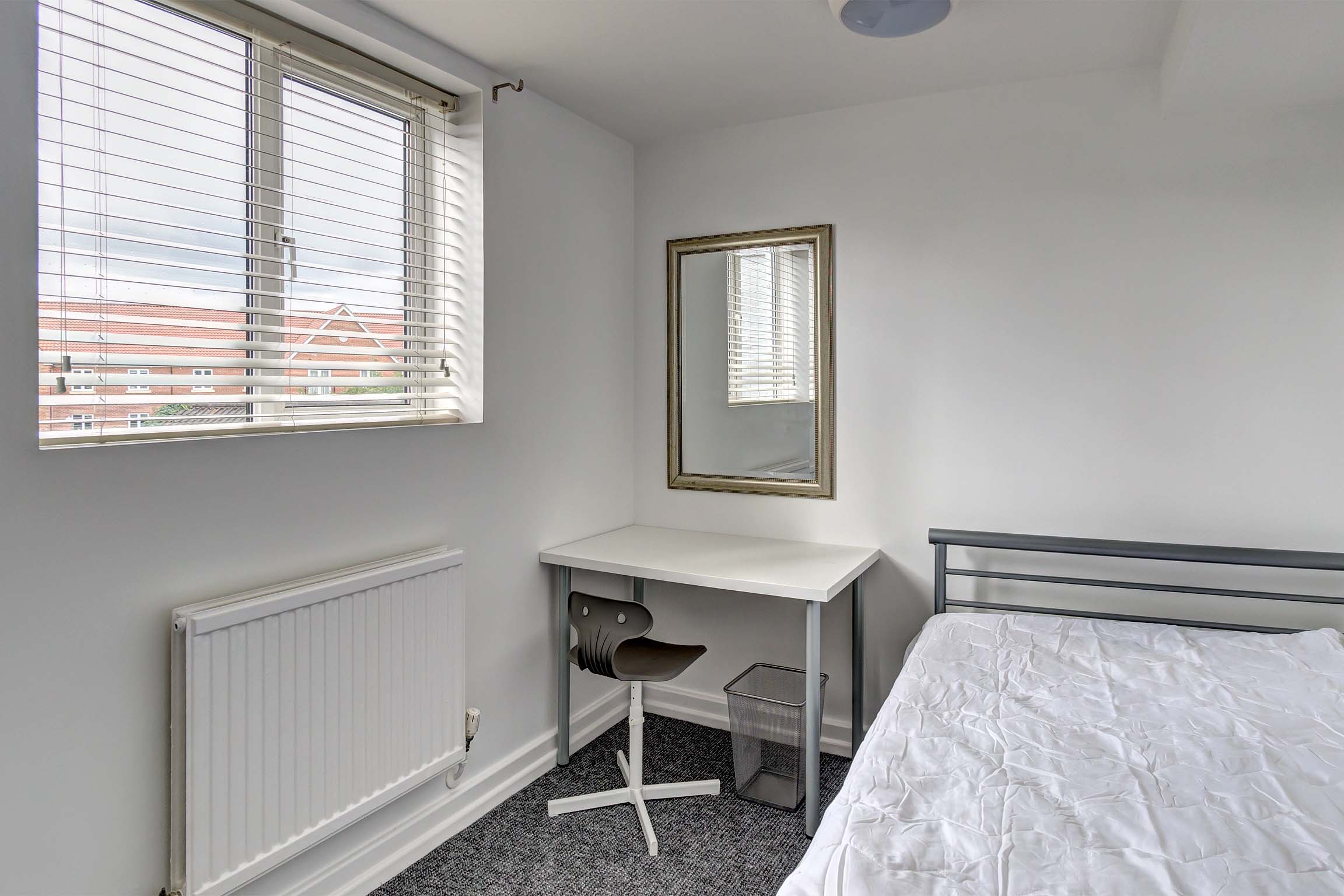 Double bedroom with metal bedframe and white desk.