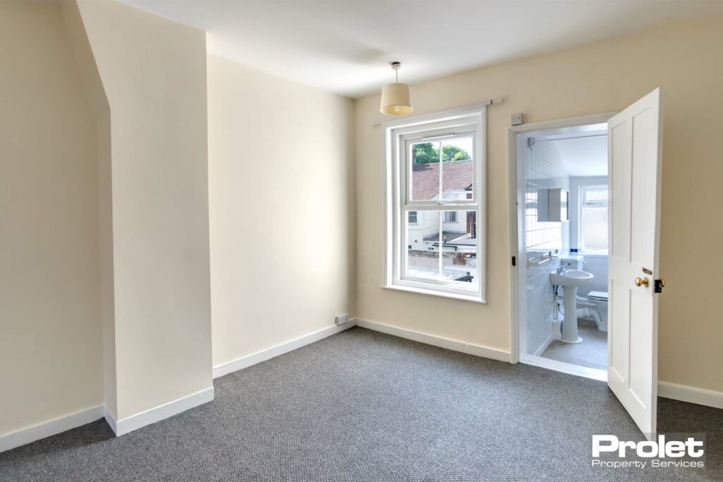 Magnolia walls and grey carpet with one window leading off to bathroom