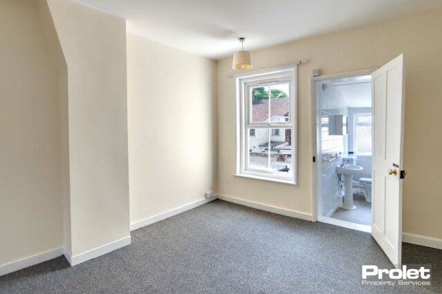 Magnolia walls and grey carpet with one window leading off to bathroom
