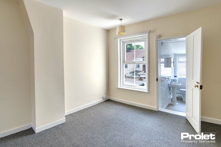 Magnolia walls and grey carpet with one window leading off to bathroom