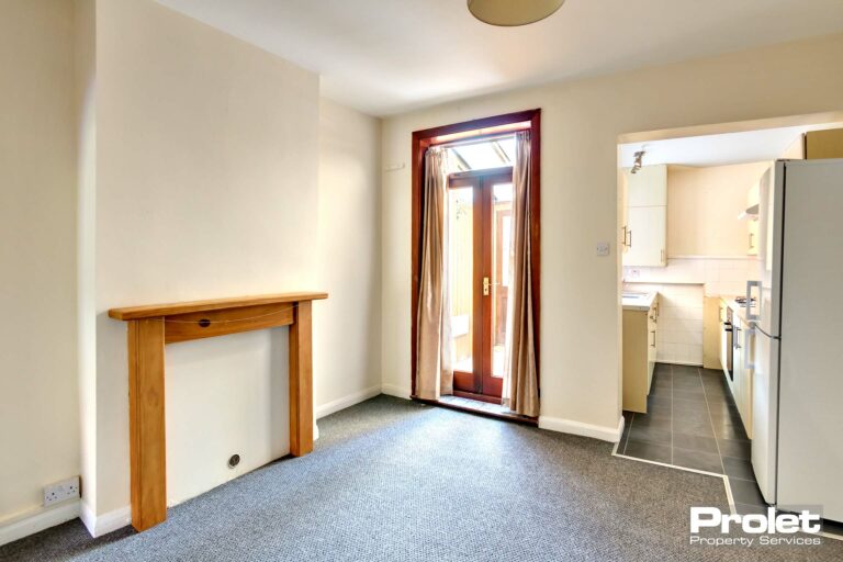 Magnolia walls, grey carpet. curtians to windows and pine feature fireplace surround. Door leading to rear lean to.