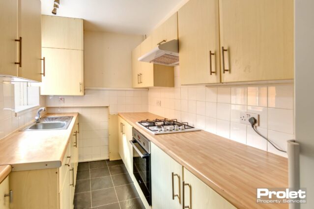 Grey floor with white tiles with wooden effect work top and units. Built in oven and hob and freestanding fridge freezer.