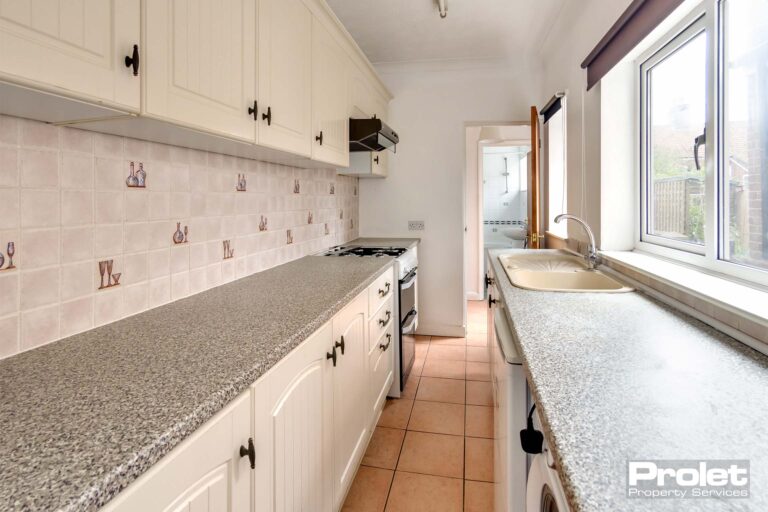 Galley kitchen with white cabinets and grey worktops.