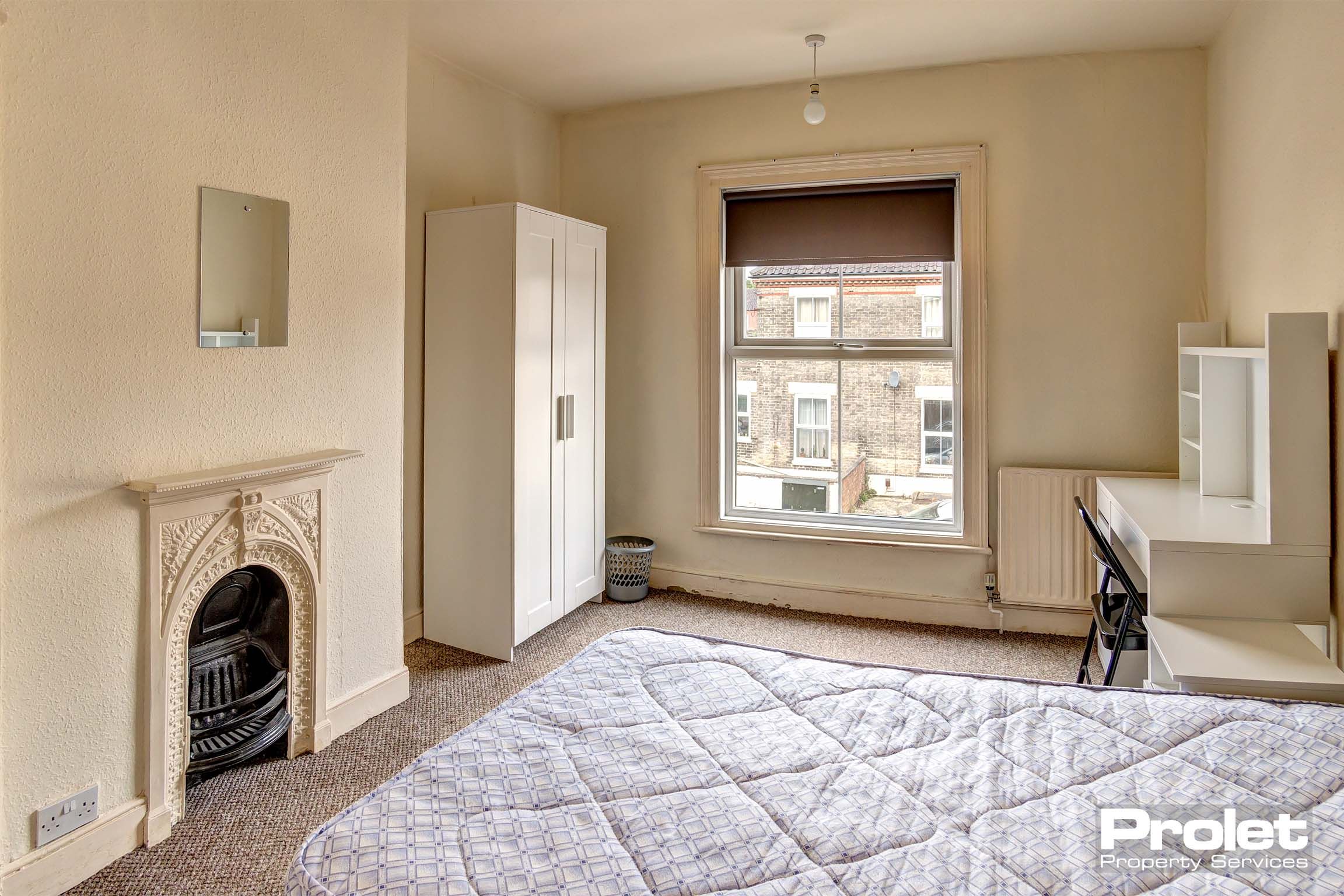 Double bedroom with a light brown carpet, magnolia walls, a white decorative fireplace, a white wardrobe and desk with a black chair.