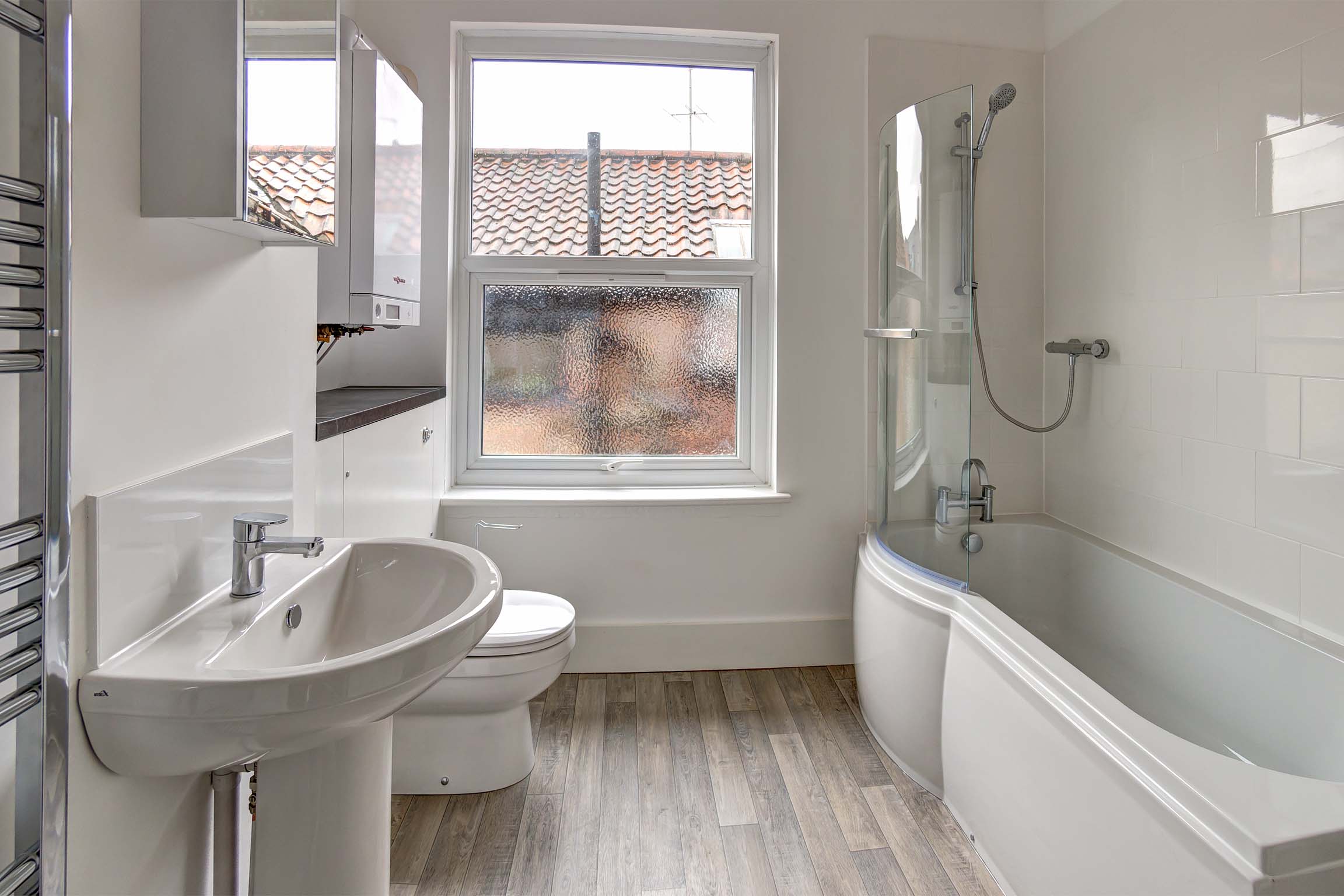 Woodne effect lamiante flooring with white suite and shower over bath