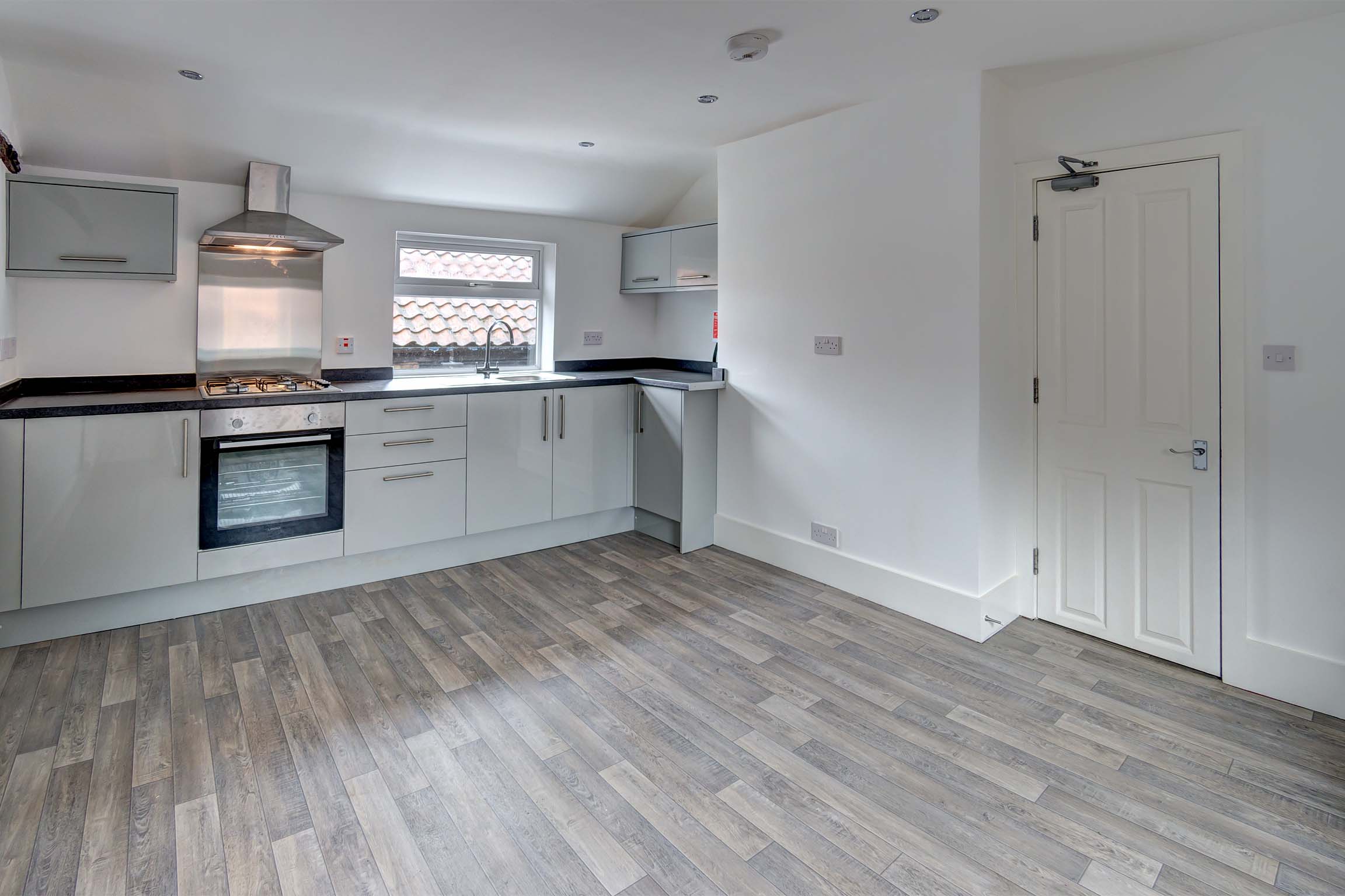 Modern kitchen with wooden effect laminate flooring, dining are, white units and walls. oven, hob and fridge with freezer box