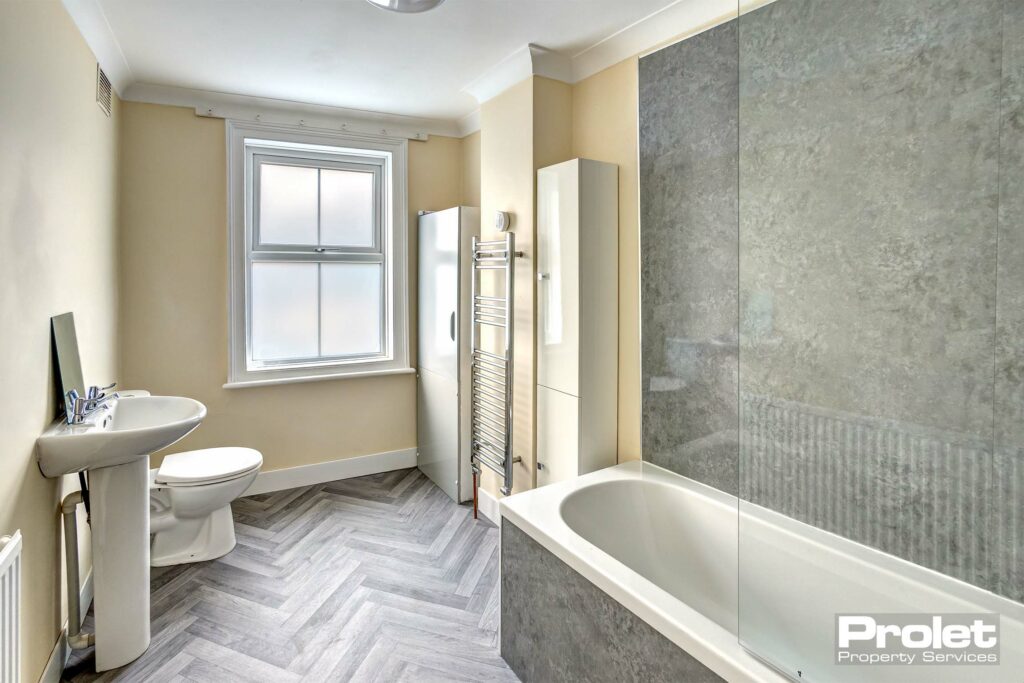 Modern bathroom with shower over bath, toilet, sink, storage cabinets, towel warmer, and herringbone style floor