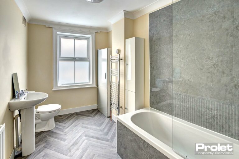 Modern bathroom with shower over bath, toilet, sink, storage cabinets, towel warmer, and herringbone style floor