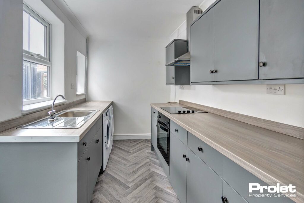 Modern kitchen with grey cabinets, wood effect worktops, and herringbone style flooring