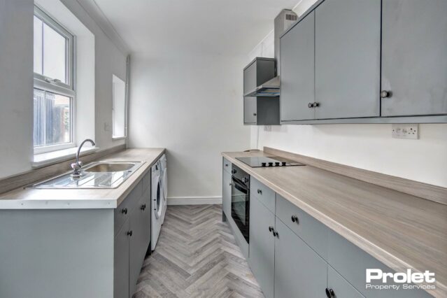 Modern kitchen with grey cabinets, wood effect worktops, and herringbone style flooring