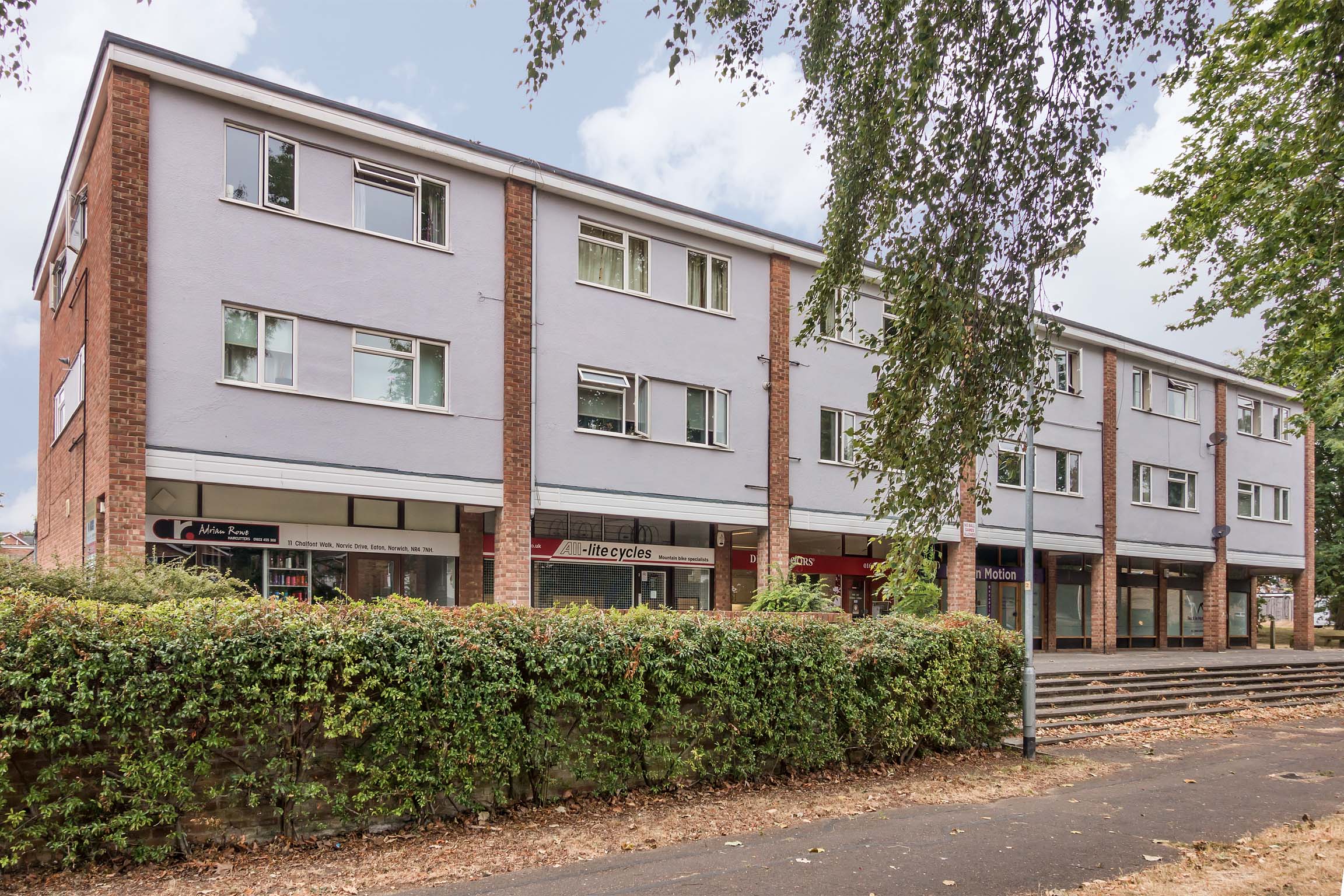 View of flats from outside, ground floor shops, with two floors of flats above.