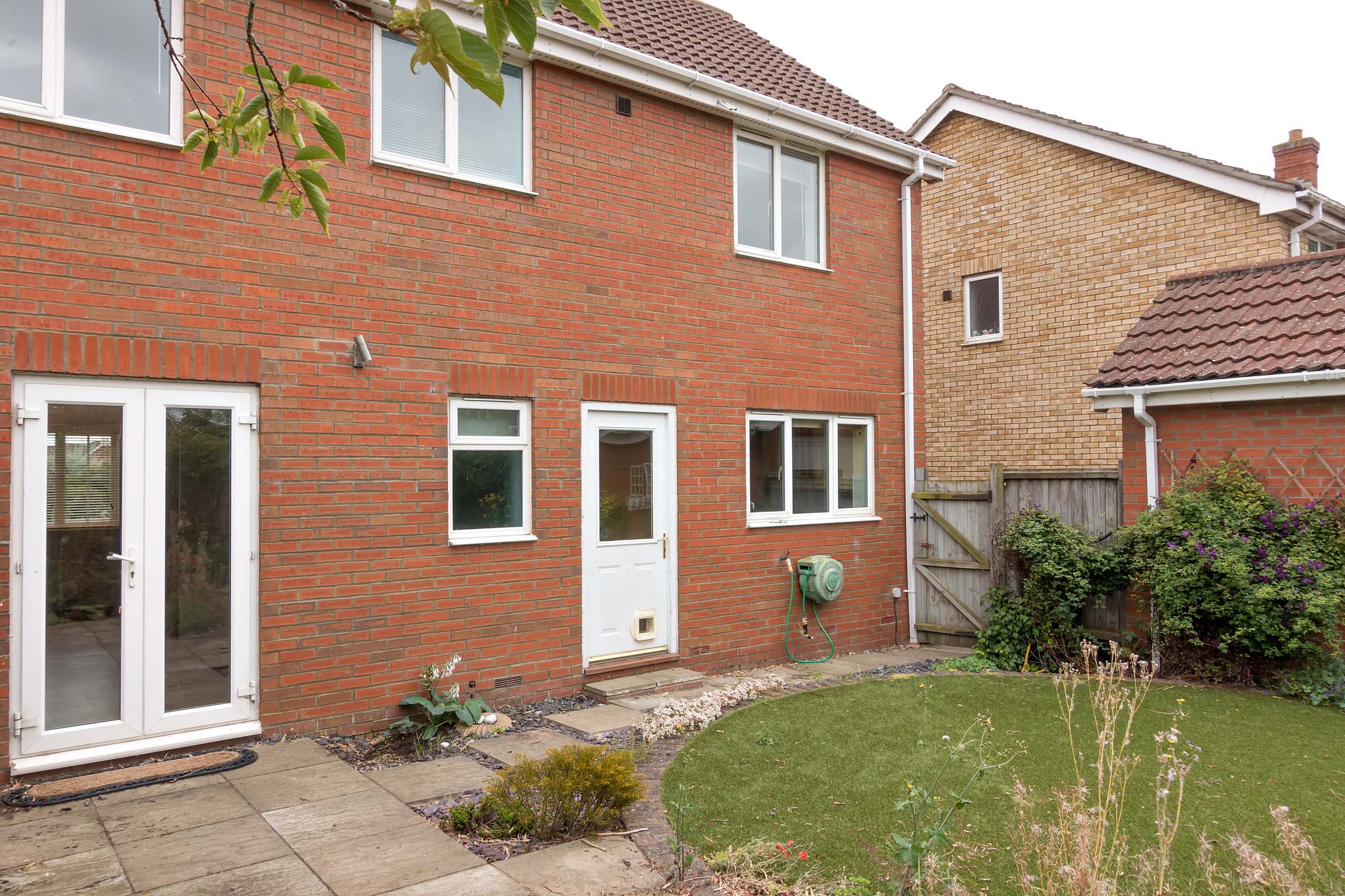 Rear view of detached brick house with garden area and french doors.