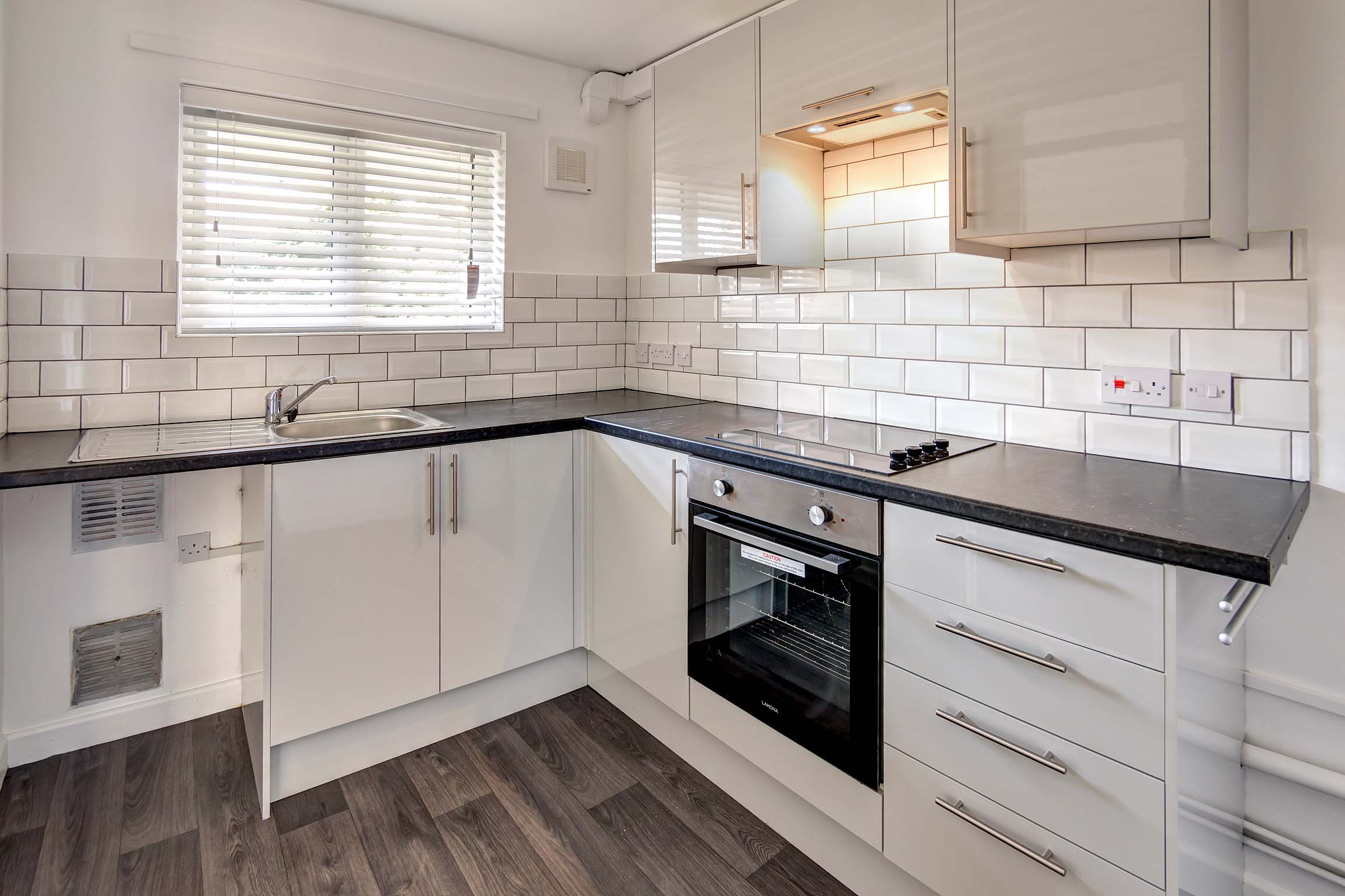 White kitchen units with white tiled walls wood effect floor. Built in hob and space for washing machine and fridge freezer.