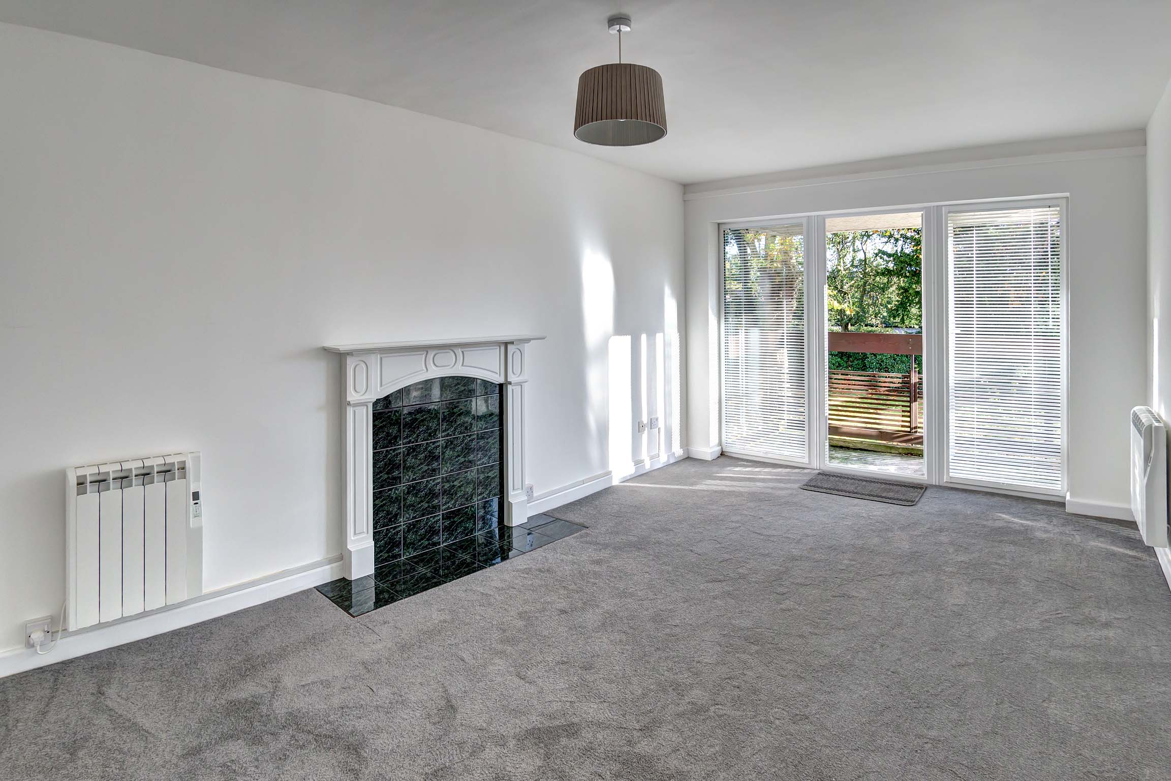 White walls and grey carpets with feature fireplace and door to balcony