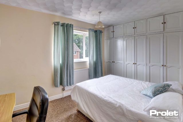 Large bedroom with magnolia walls and built in white wardrobes and high cupboards.