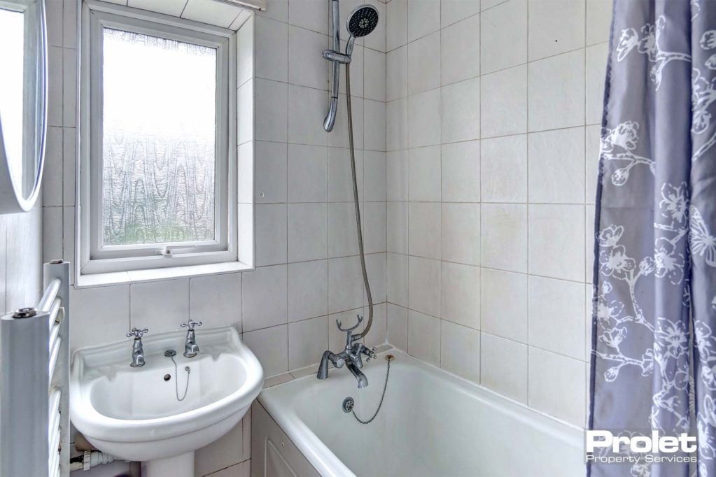 Tiled bathroom with shower over a white bath tub, a white sink and a wall radiator for towels.