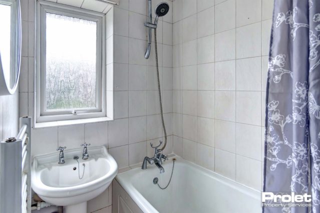 Tiled bathroom with shower over a white bath tub, a white sink and a wall radiator for towels.
