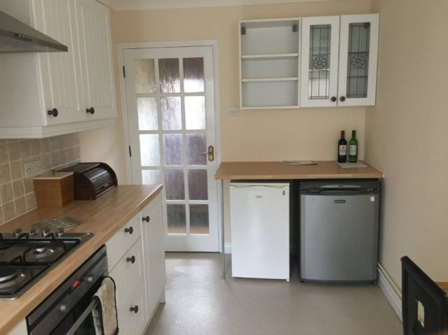 Kitchen with white fitted units and wooden effect worktop. An oven and undercounter fridge and freezer.