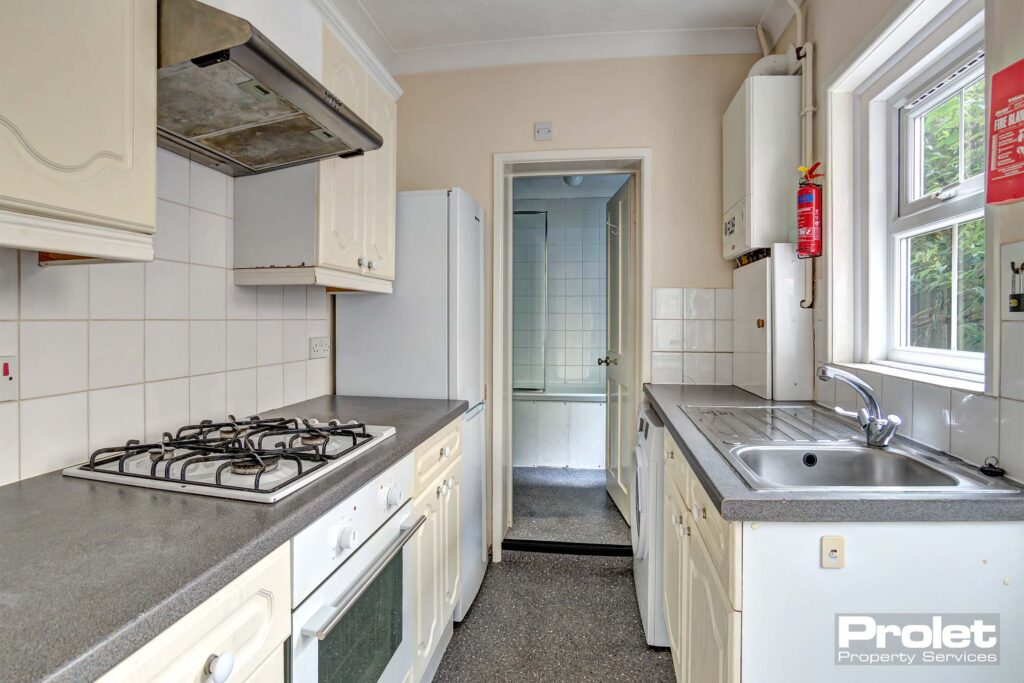 Kitchen with white goods leading to bathroom and back door to garden