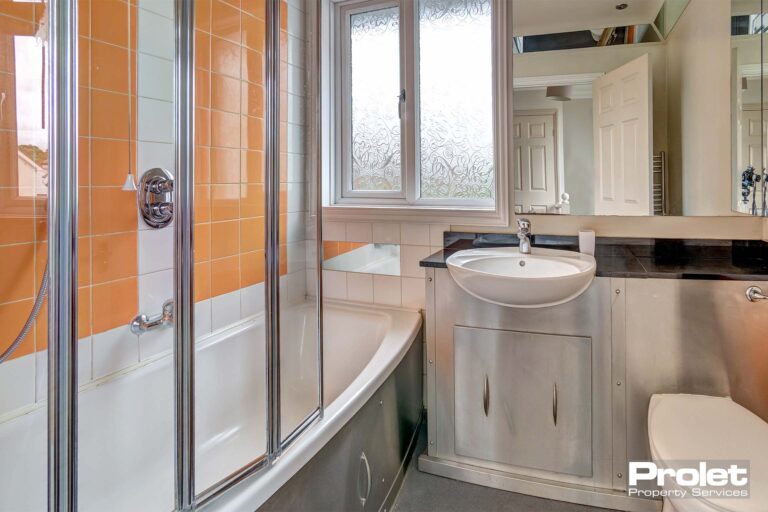 Bathroom with white toilet and sink with cupboard storage under the sink. A white bath tub with a glass splash guard for the shower above the bath.