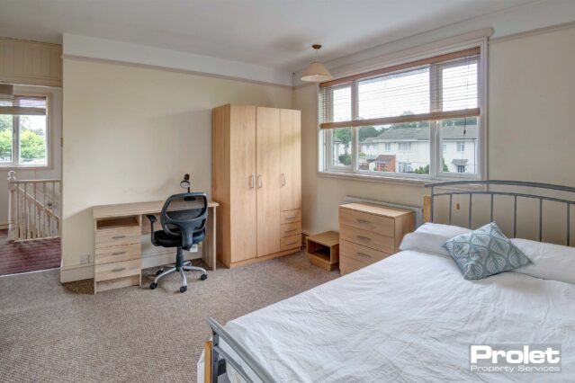 Double bedroom with brown carpet, a metal bedframe, a wooden wardrobe, beside table and a wooden desk with a black chair.