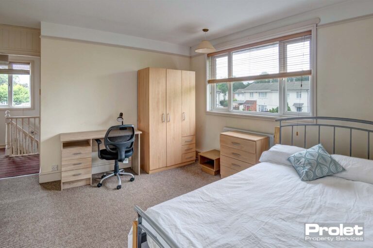 Double bedroom with brown carpet, a metal bedframe, a wooden wardrobe, beside table and a wooden desk with a black chair.