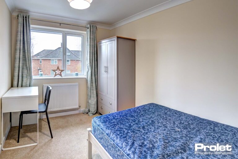 Double bedroom with neutral coloured carpet, a white desk with black chair. A door for access to the ensuite bathroom.