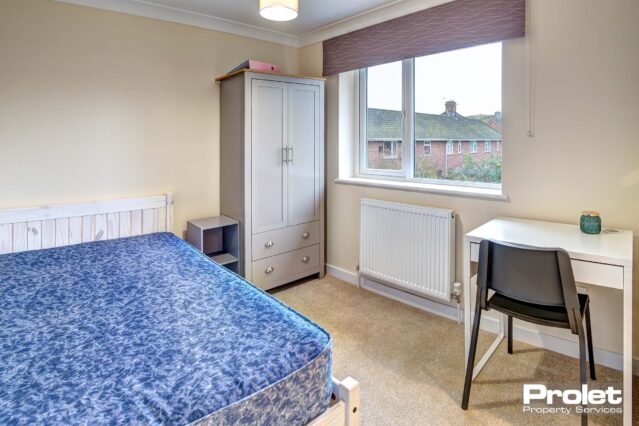 Double bedroom with neutral coloured carpet, a white desk with black chair. A door for access to the ensuite bathroom.