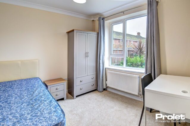Double bedroom with neutral coloured carpet, a white desk with black chair. A door for access to the ensuite bathroom.