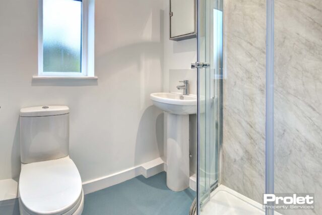Ensuite bathroom with walk in shower with glass doors, a white toilet and sink.