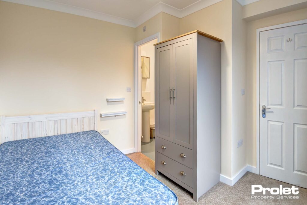 Double bedroom with neutral coloured carpet, a white desk with black chair. A door for access to the ensuite bathroom.