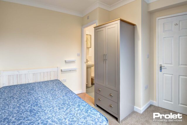 Double bedroom with neutral coloured carpet, a white desk with black chair. A door for access to the ensuite bathroom.