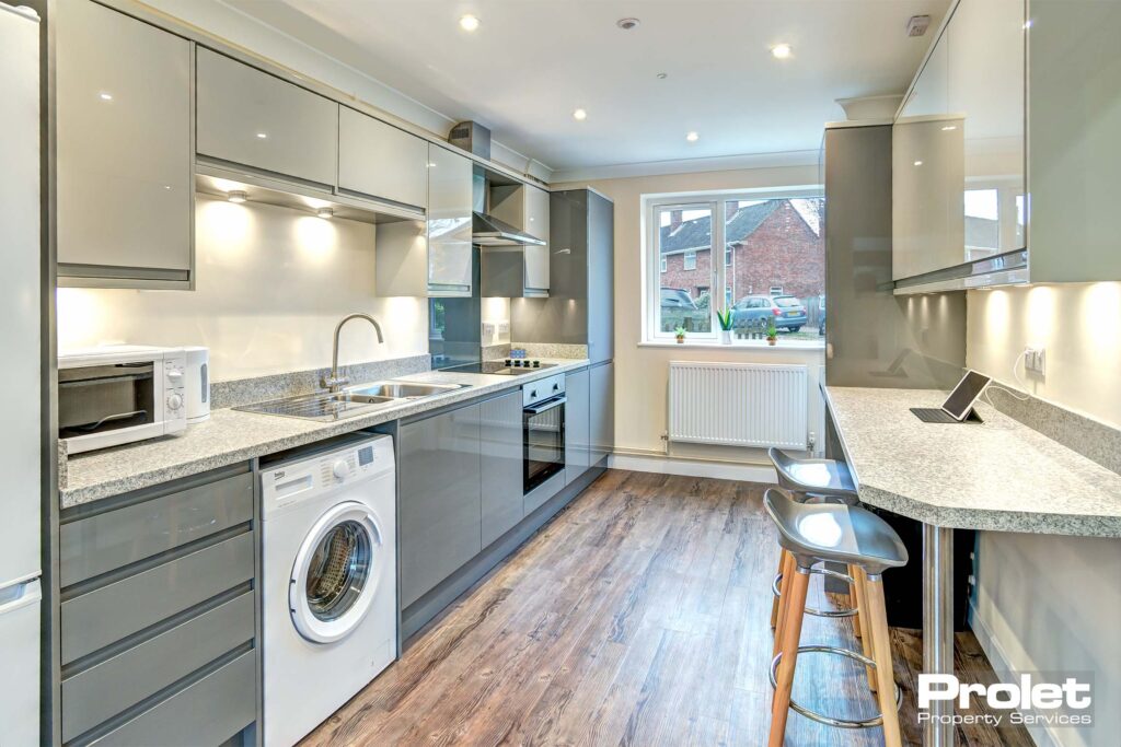 Large kitchen area with wooden effect lino flooring. A dark grey fitted kitchen with a marble breakfast bar and two chairs.
