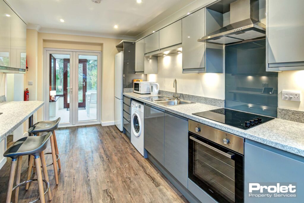 Large kitchen area with wooden effect lino flooring. A dark grey fitted kitchen with a marble breakfast bar and two chairs.