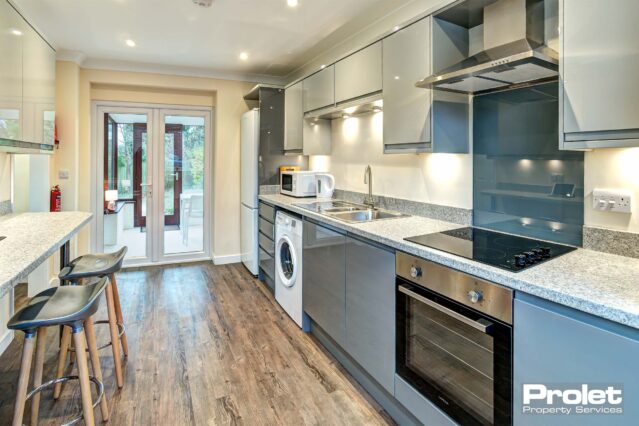Large kitchen area with wooden effect lino flooring. A dark grey fitted kitchen with a marble breakfast bar and two chairs.