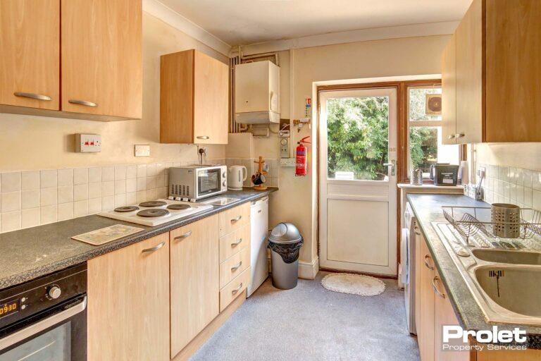 Kitchen with wood cabinets, grey worktops, and white goods