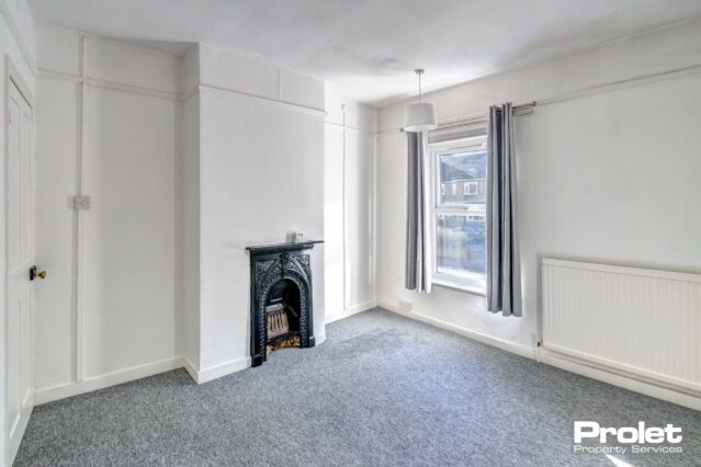 Bedroom with walls painted off white with grey carpet and feature fireplace.