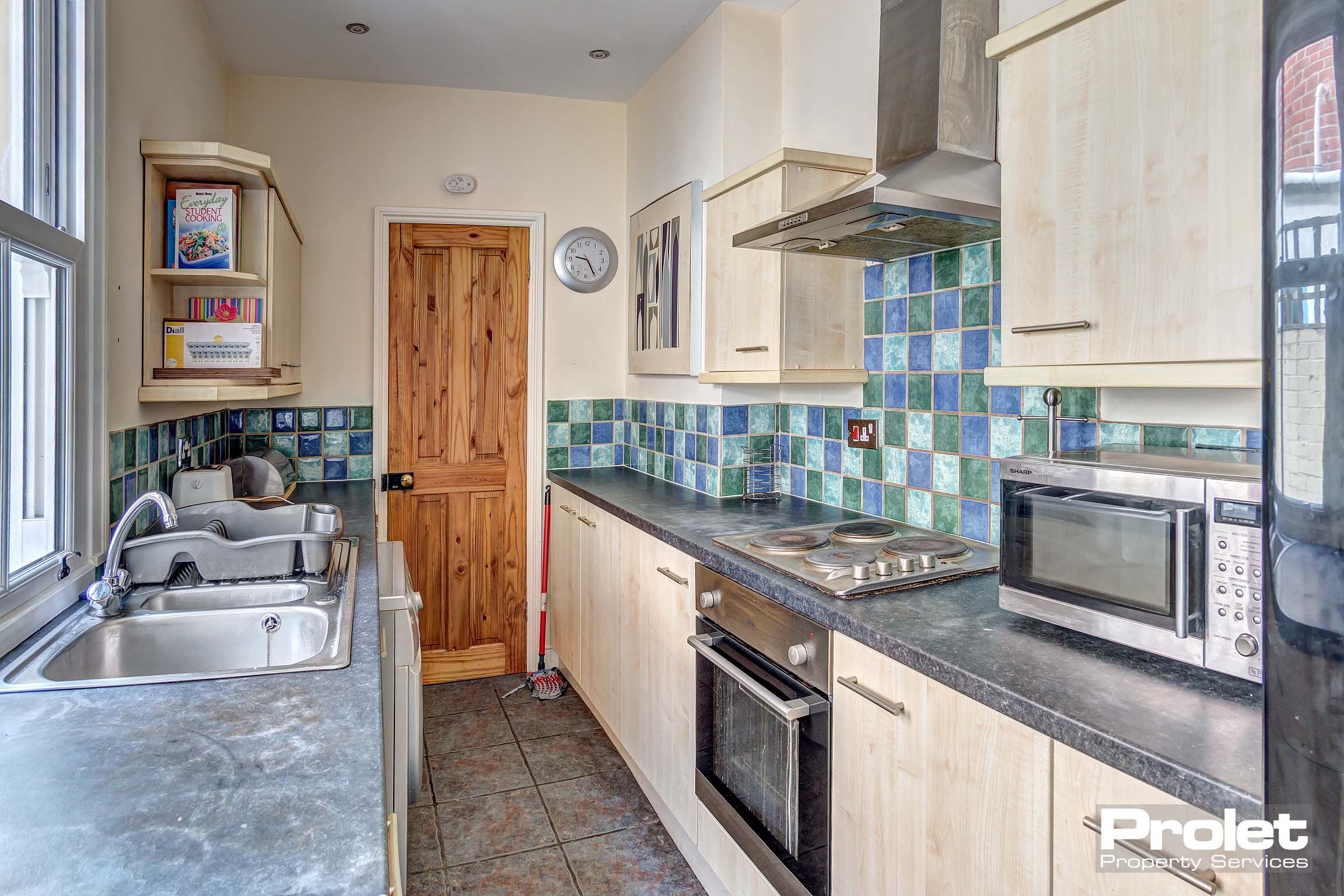 Galley kitchen with blue tiled backsplash, wood effect cabinets, and large appliances
